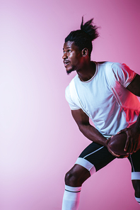 handsome african american sportsman playing american football on purple background with gradient