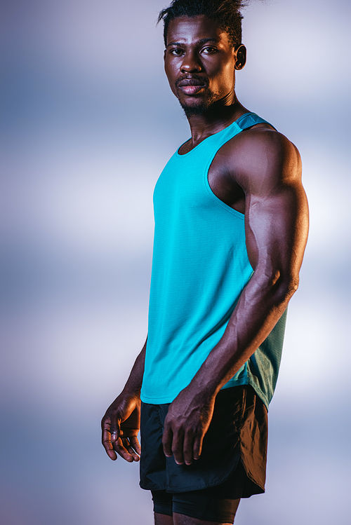handsome, athletic african american sportsman  on grey and blue background with lighting