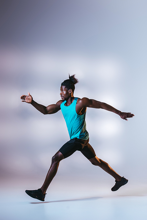 young african american sportsman running on grey background with lighting