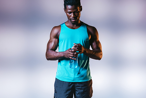 serious african american sportsman holding sports bottle on grey background with lighting