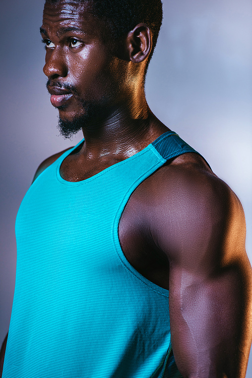 confident, athletic african american sportsman looking away on grey and blue gradient background with lighting