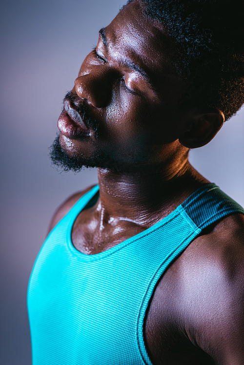 portrait of african american sportsman with sweaty face and closed eyes on grey background with lighting