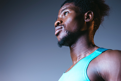handsome, confident african american sportsman looking away on grey background with lighting