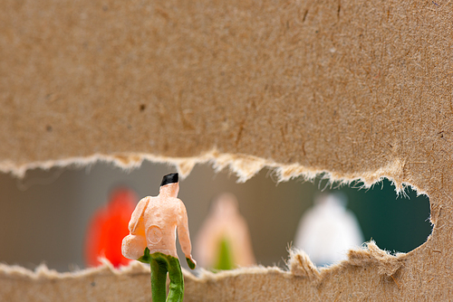 Selective focus of doll near hole in cardboard with silhouettes of people figures at background