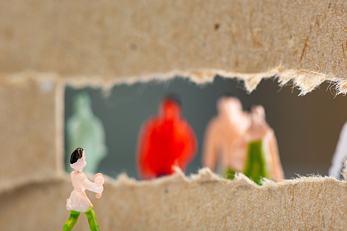 Selective focus of toy near hole in cardboard with silhouettes of people figures at background