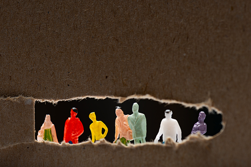 Selective focus of cardboard with hole and people figures isolated on black, concept of social equality