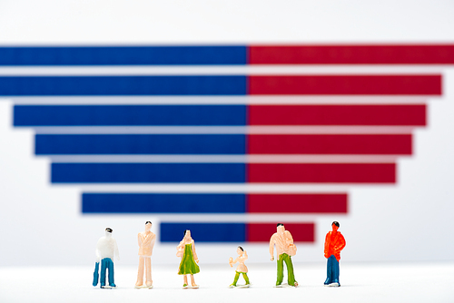 Selective focus of plastic people figures on white surface near blue and red graphs at background, concept of equality