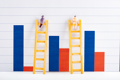 People figures on ladders on white surface near blue and red graphs at background, equality concept