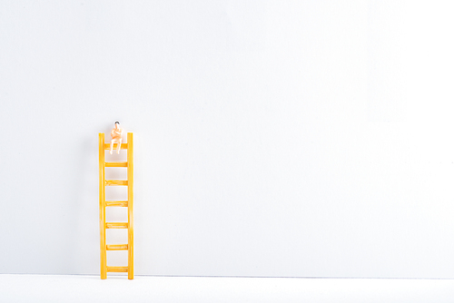 Doll on ladder on white surface on grey background, concept of equality rights