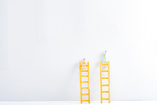 Plastic people figures on ladders on white surface on grey background, concept of equality rights