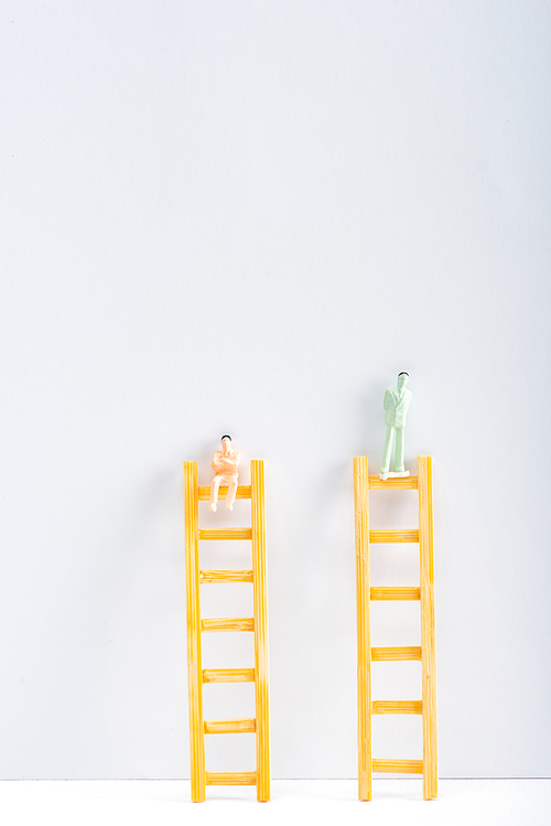 Two people figures on ladders on white surface on grey background with copy space, concept of equality rights