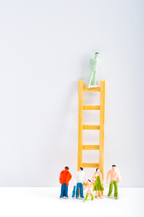 Doll on ladder with people figures on white surface on grey background, concept of equality rights