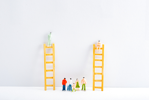 Dolls on ladders with people figures on white surface on grey background, concept of equality rights