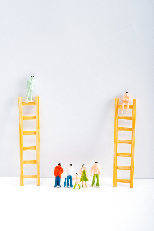 Plastic people figures near dolls on ladders on white surface on grey background, concept of equality rights