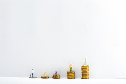 Plastic people figures on stacked coins on white surface on grey background, concept of financial equality