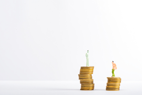 Two people figures on stacked coins on white surface isolated on grey, concept of financial equality