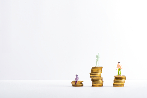 Three people figures on stacked coins on white surface isolated on grey, concept of financial equality