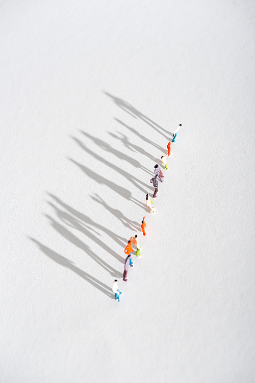Top view of row of plastic people figures with shadow on white surface