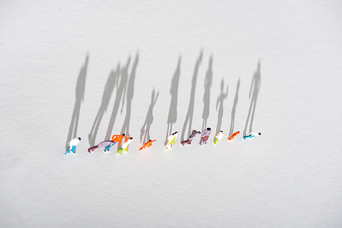 Top view of row of plastic people figures on white surface with shadow