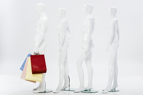 row of white mannequins with shopping bags on grey