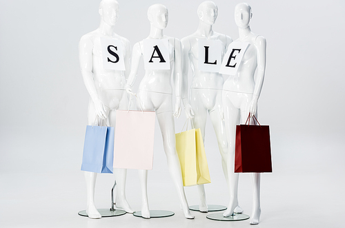 white mannequins with sale lettering on papers and shopping bags isolated on grey