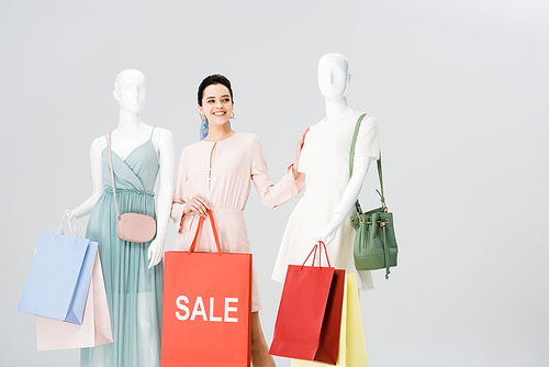 beautiful young woman with sale lettering on shopping bag near mannequins isolated on grey