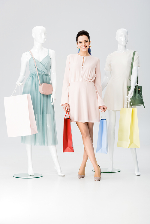 beautiful smiling young woman with shopping bags near mannequins on grey