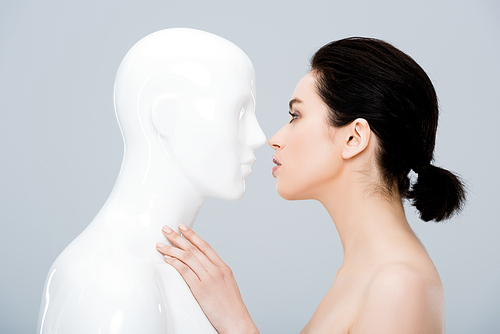beautiful young woman looking at plastic mannequin isolated on grey