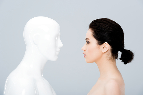 beautiful young woman looking at plastic mannequin isolated on grey