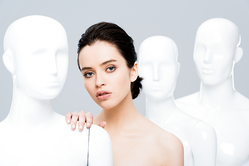 beautiful young woman posing with mannequins isolated on grey