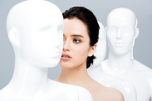 beautiful girl posing in row of mannequins isolated on grey