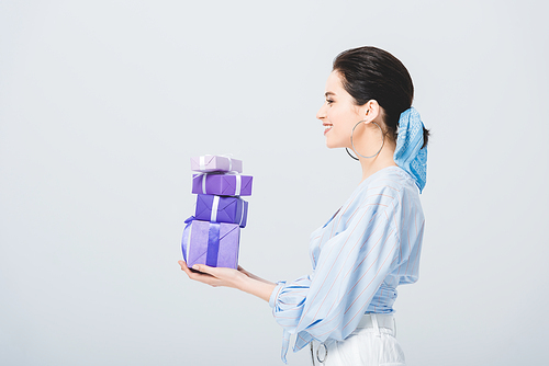 side view of beautiful stylish girl holding gift boxes isolated on grey