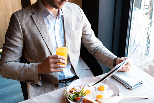 cropped view of businessman holding glass of orange juice and newspaper in cafe