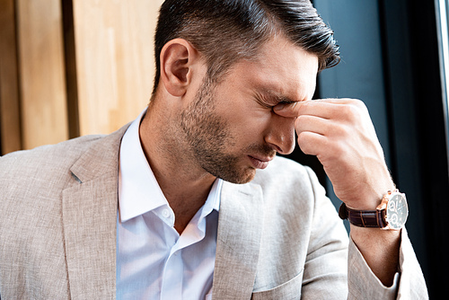 tired businessman touching nose with closed eyes in cafe