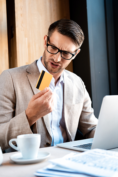 confused businessman in glasses with credit card and laptop in cafe