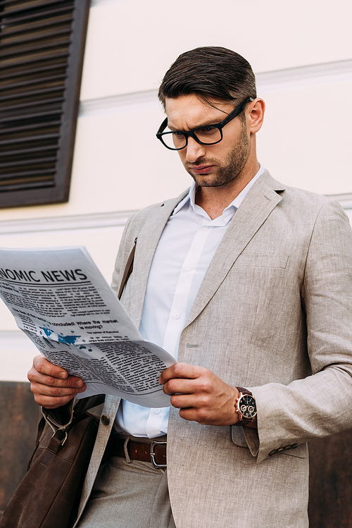 focused businessman in glasses reading newspaper on street