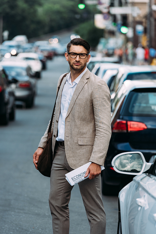 serious man in glasses holding newspaper on street with cars