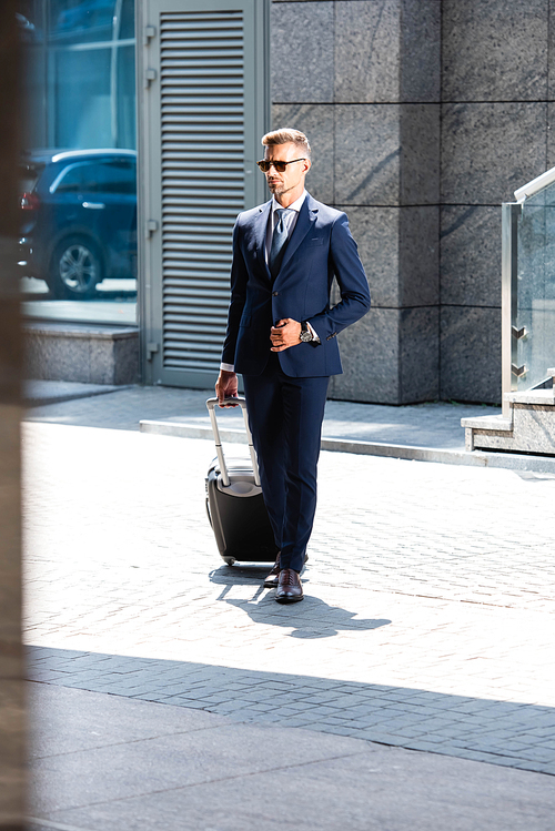 handsome man in suit and glasses holding suitcase and looking way
