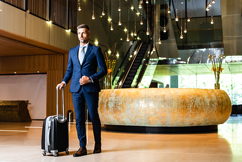 handsome businessman in suit holding suitcase and looking away