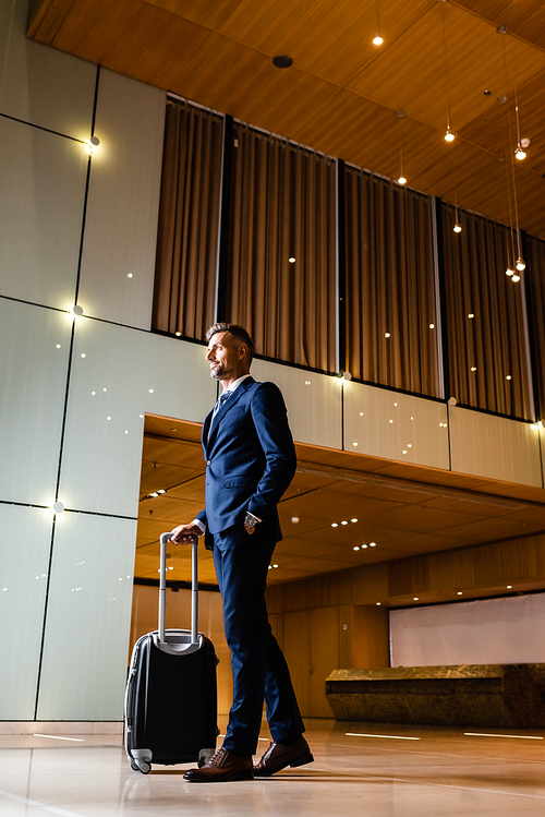 handsome businessman in suit with hand in pocket holding suitcase