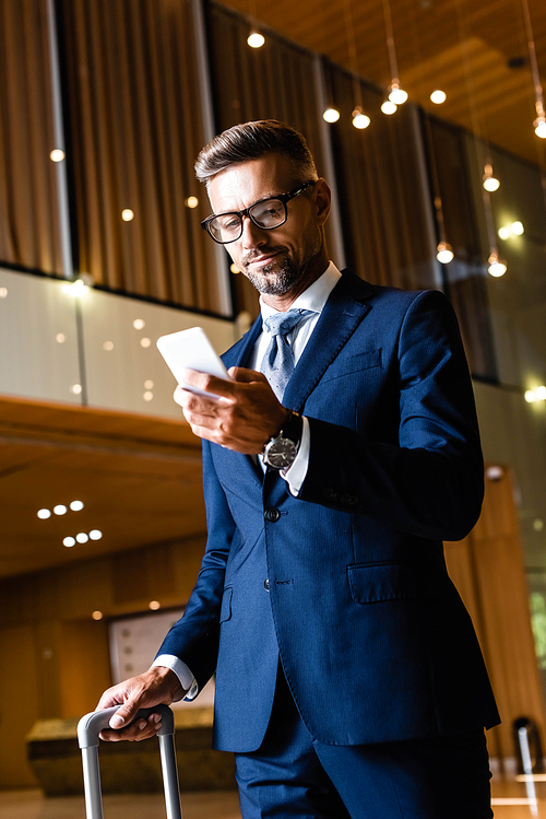 handsome businessman in suit and glasses using smartphone in hotel