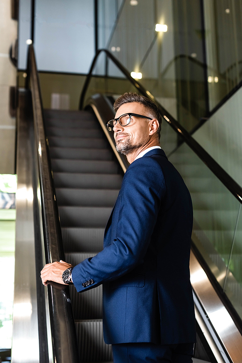 handsome and confident businessman in suit and glasses on escalator