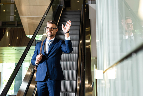 handsome businessman in suit and glasses waving in hotel