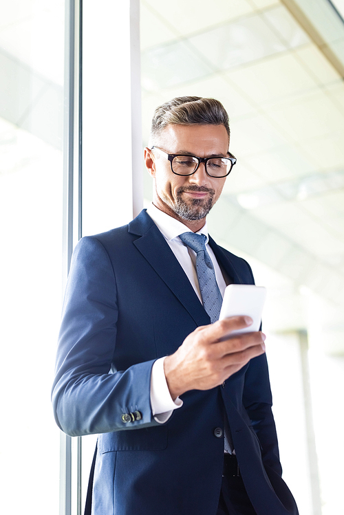handsome businessman in formal wear and glasses using smartphone