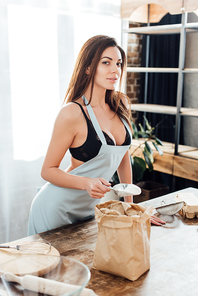 Sexy woman in underwear and blue apron with flour in paper bag in kitchen