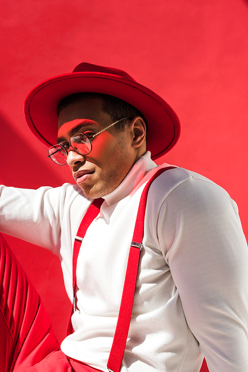 유토이미지 | fashionable mixed race man in hat, glasses and suspenders posing on red