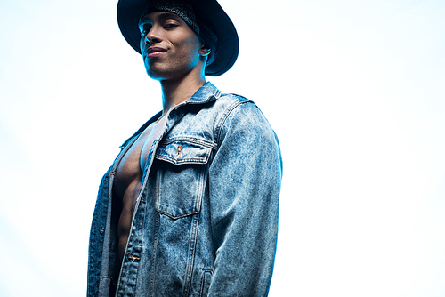 handsome stylish mixed race man in denim and hat posing isolated on blue with copy space