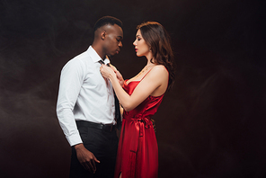 beautiful woman in red dress undressing shirt of african american man isolated on black with copy space