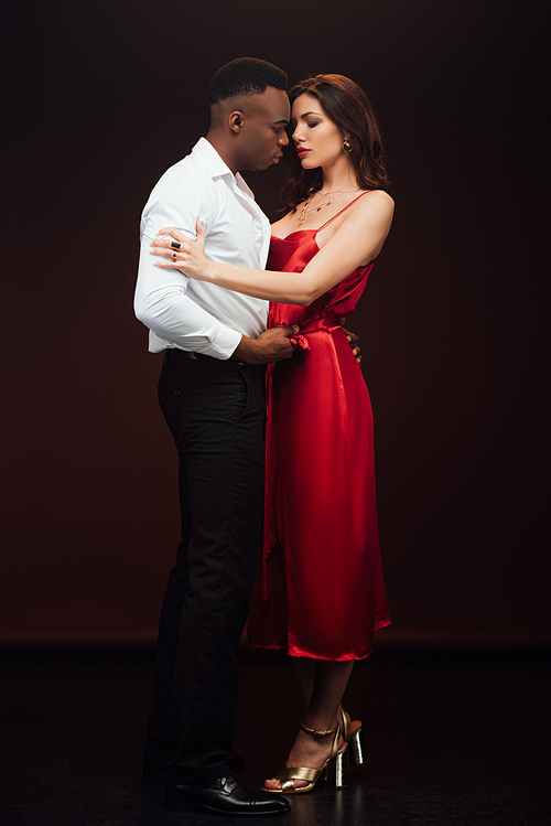 handsome african american man embracing beautiful woman in red dress isolated on black