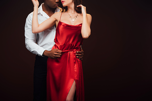 partial view of african american man embracing woman in red dress isolated on black with copy space